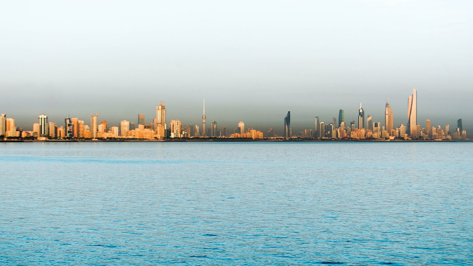 The Kuwait City skyline seen across the bay at first light, its towers catching the early sun