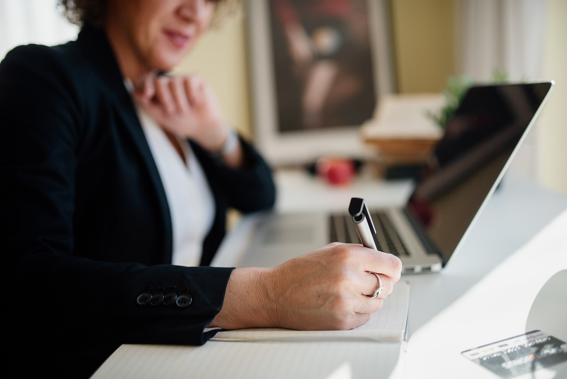 A business professional taking notes at a modern office desk beside a laptop