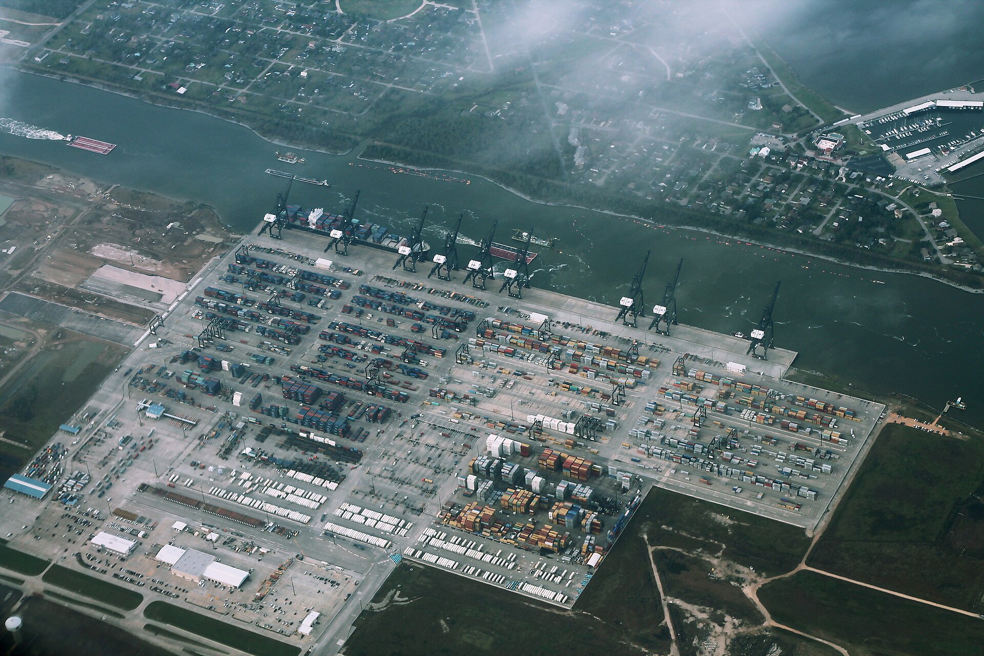 Aerial view of a container terminal with quay cranes, stacked containers and truck lanes beside a shipping channel