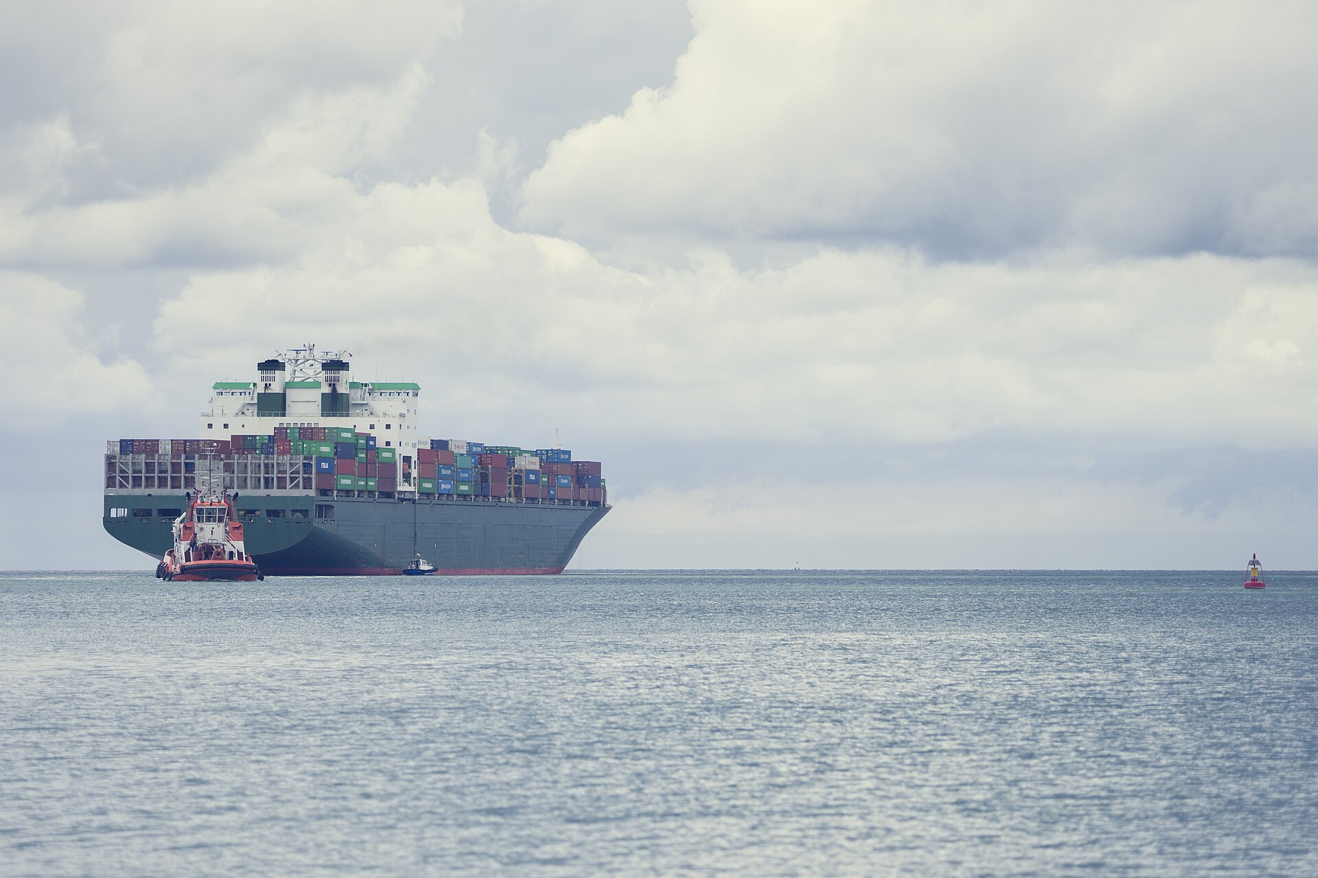 A loaded container ship arriving at port with a tugboat escorting it alongside